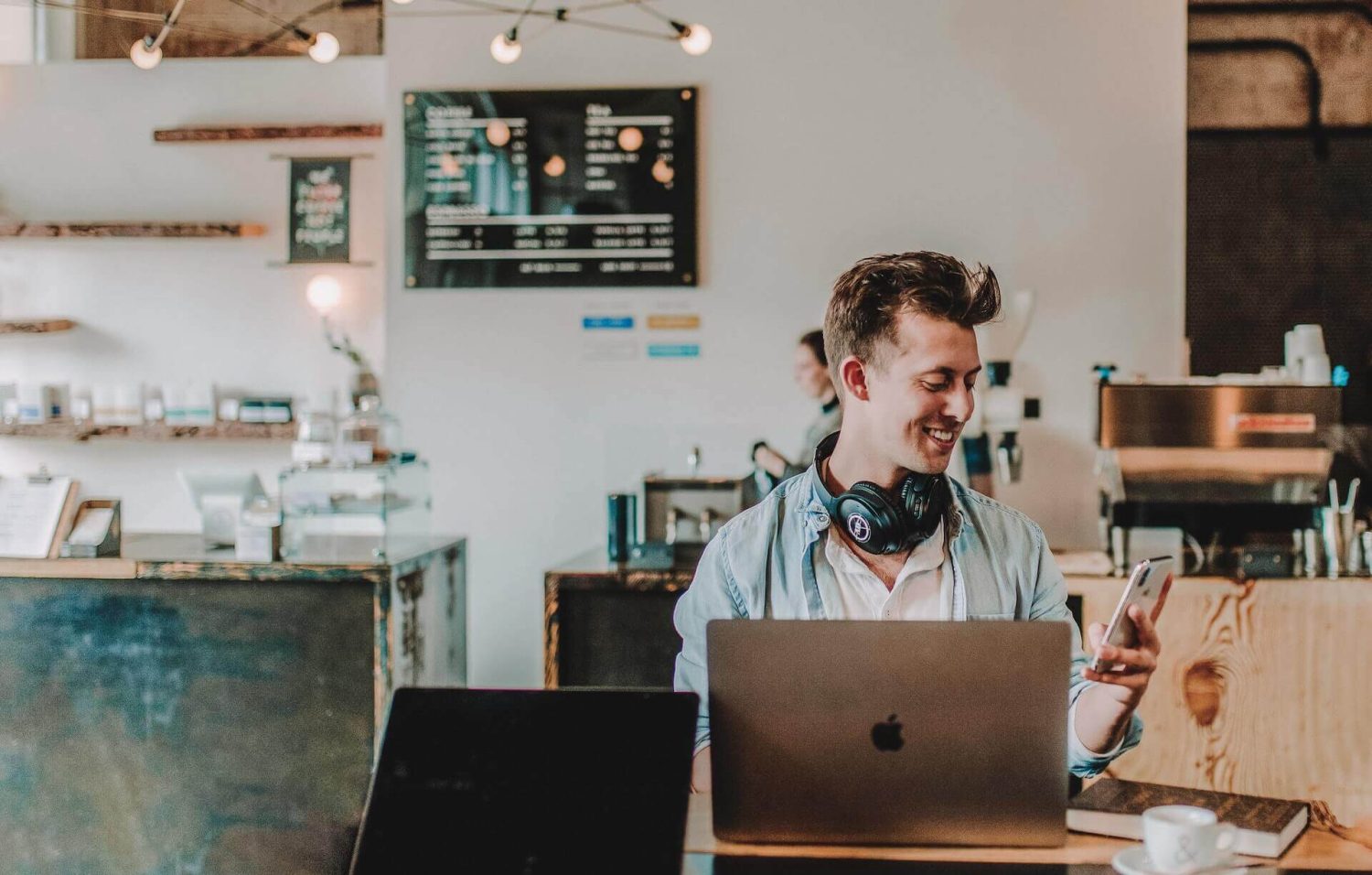 Male at a coffee shop smiling at the phone while finishing Tasks on the computer.