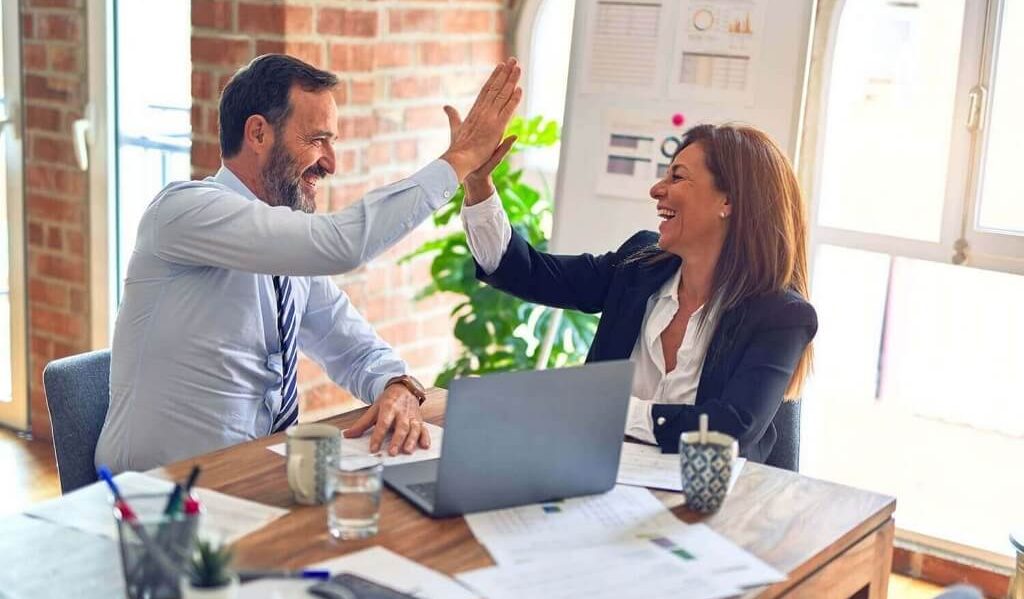 Two middle age business workers smiling happy and confident. Working together with smile on face hand giving high five at the office.