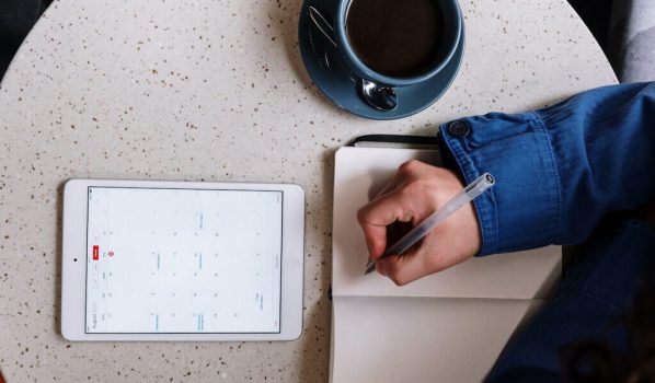 Person Holding Pen and Checking Calendar on Tablet - Doing Tasks