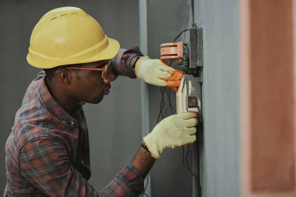 Man wearing a yellow hat and working in maintenance is fixing a machine