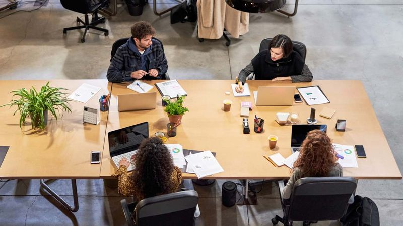 Four employees sitting in one desk with laptops and papers in front of them. 